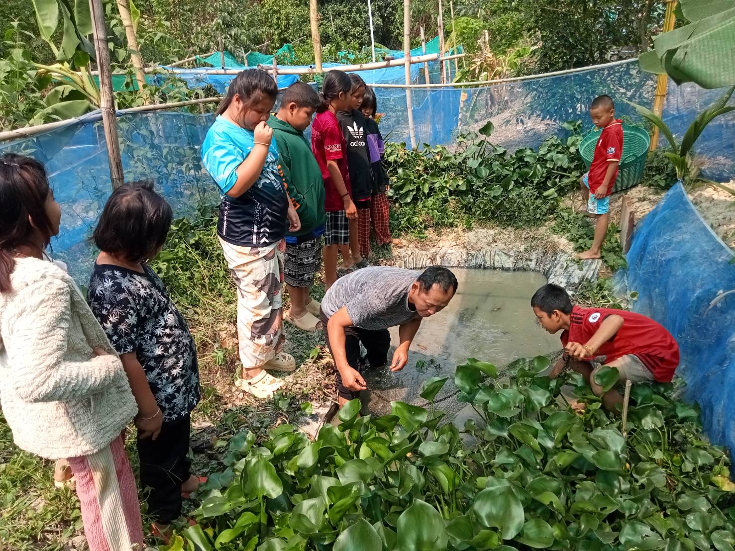 Bildet viser barn og unge som står oppstilt rundt et egengravd vannhull utendørs