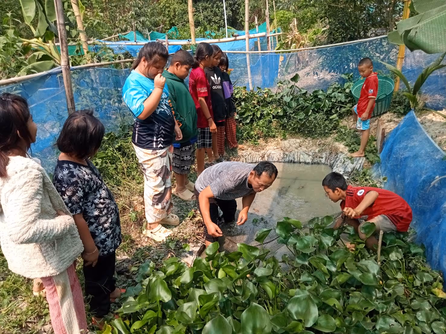 Bildet viser barn og unge som står oppstilt rundt et egengravd vannhull utendørs