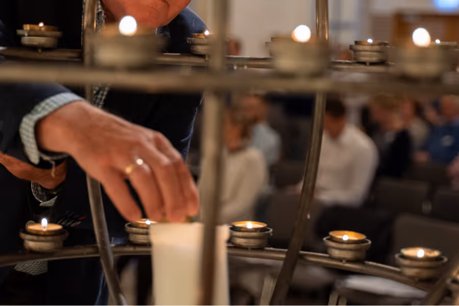 Bildet viser en hånd som tenner lys i en lysglobe i et kirkerom