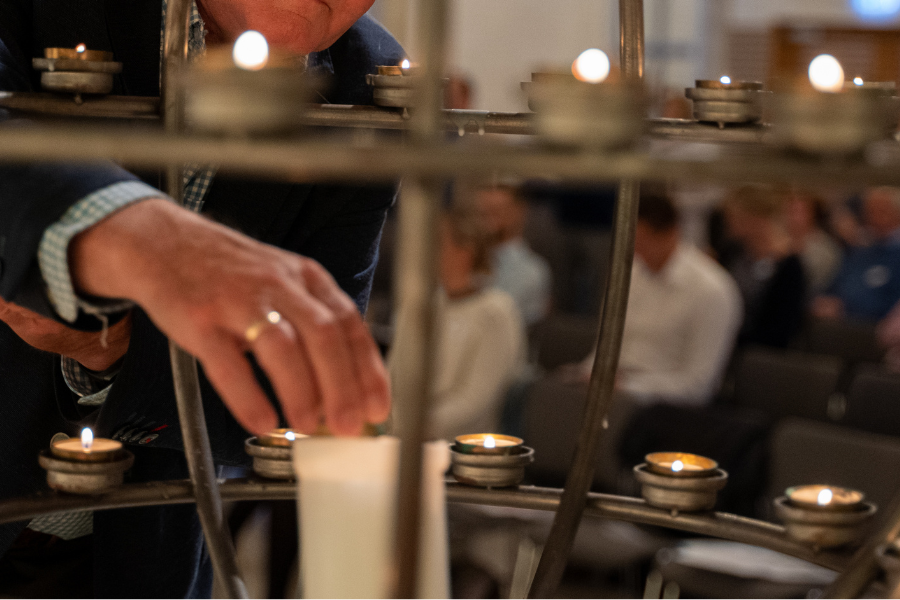 Bildet viser en hånd som tenner lys i en lysglobe i et kirkerom