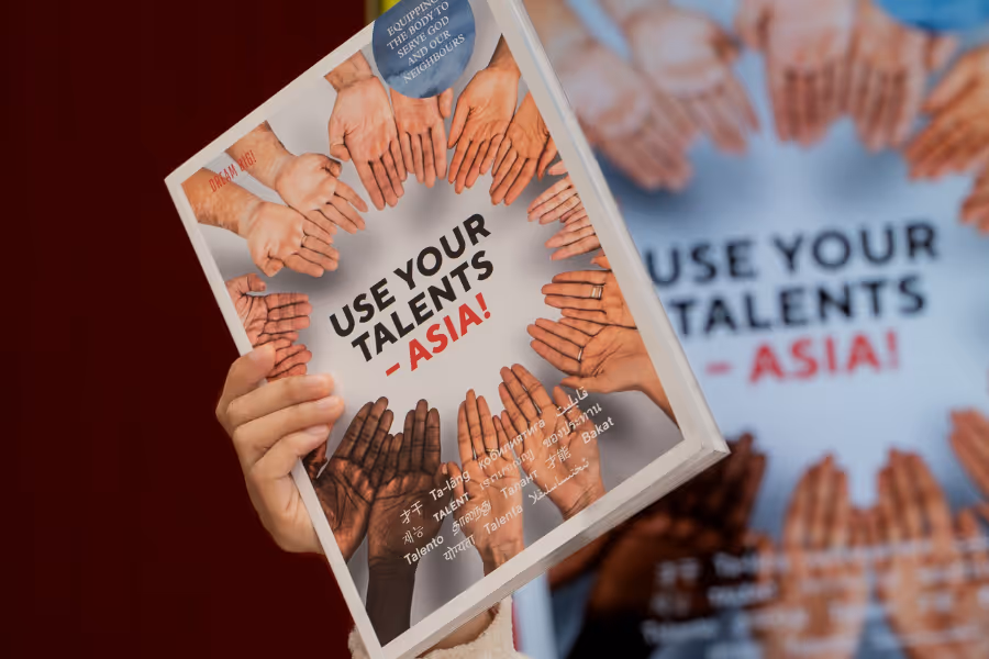 Bildet viser en hånd som holder en trykket utgave av «Use your Talents Asia»