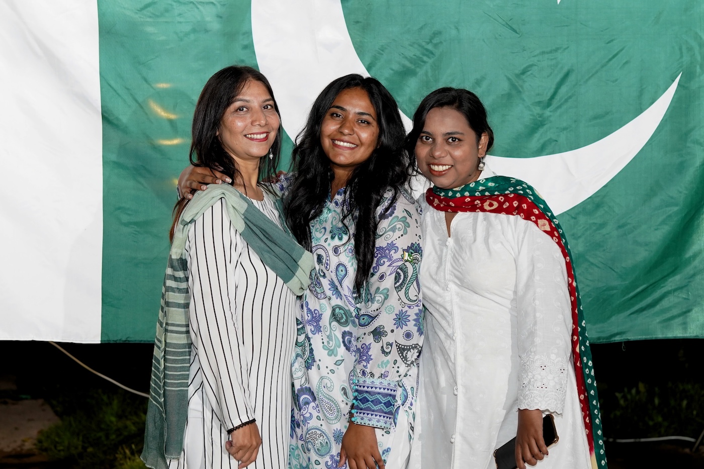 Bildet viser Gulnaz Naushad sammen med to andre kvinner foran det pakistanske flagget