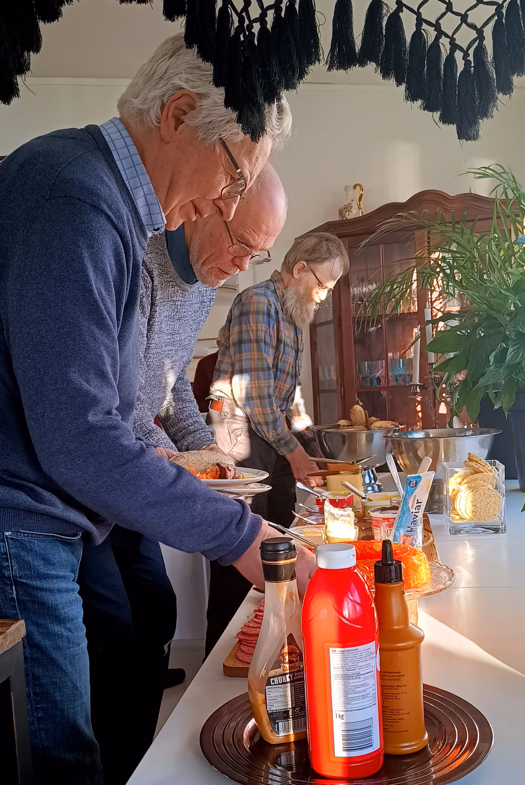 Bildet viser tre personer som forsyner seg fra et matbord