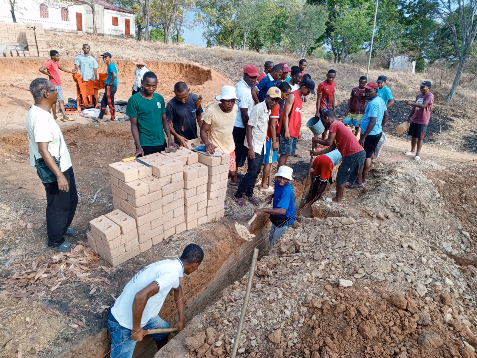 Bildet viser en gjeng som graver i en grøft. Ved siden av grøften står en stabel med murstein