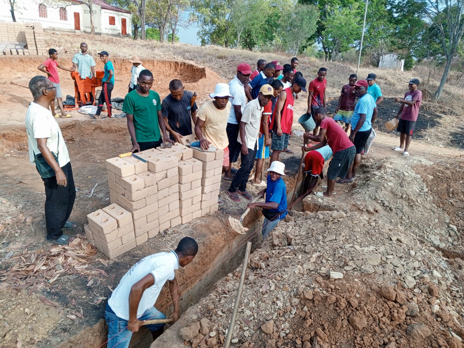 Bildet viser en gjeng som graver i en grøft. Ved siden av grøften står en stabel med murstein