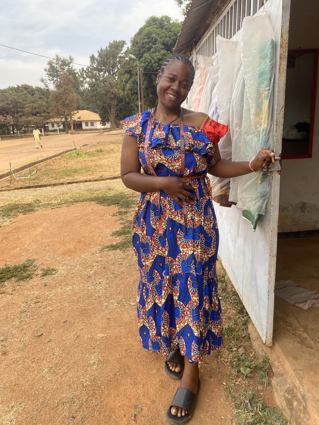 Bildet viser en kvinne i kamerunske klær som står utenfor et byggp