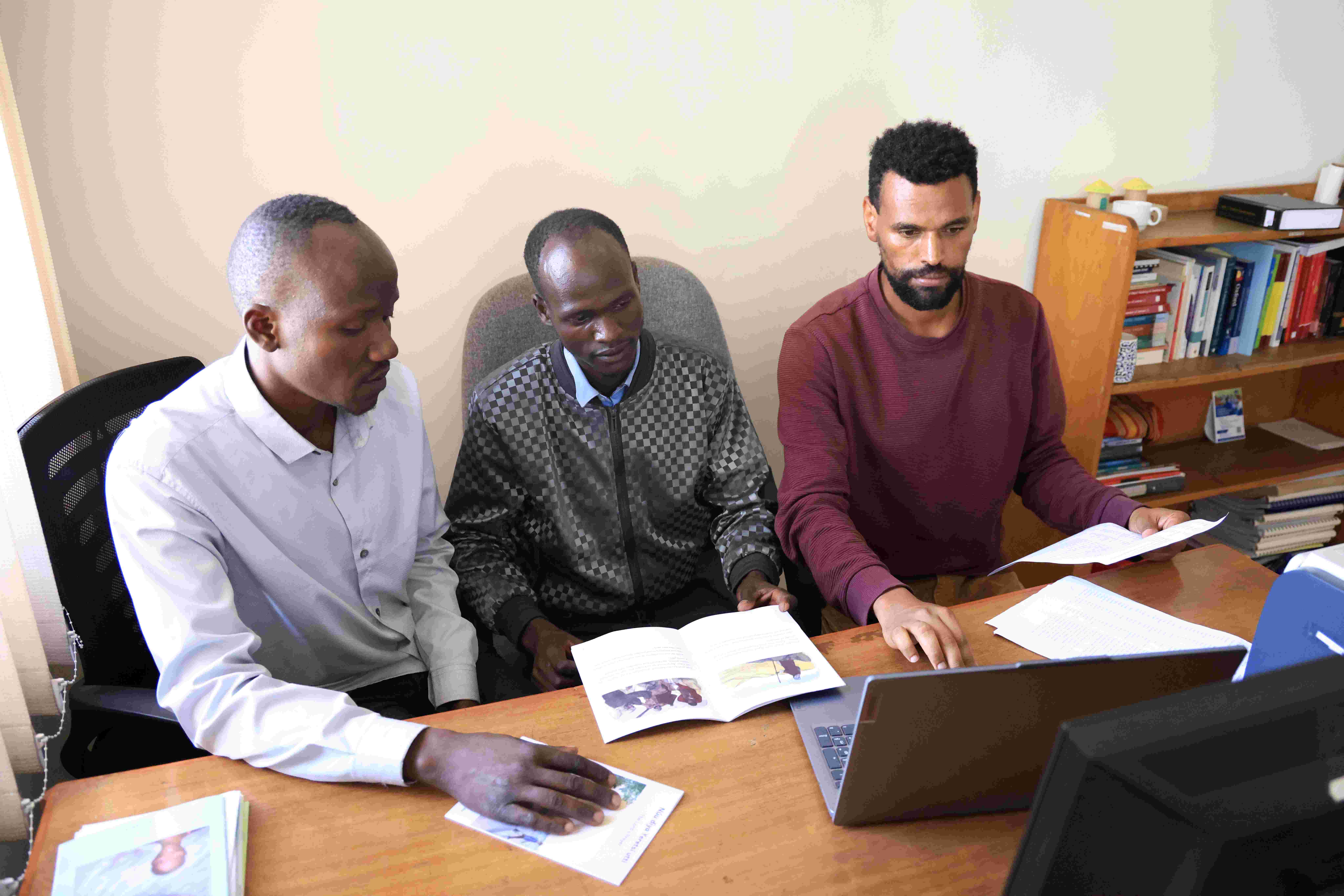 Bildet viser tre personer som jobber med tekster foran en bærbar datamaskin