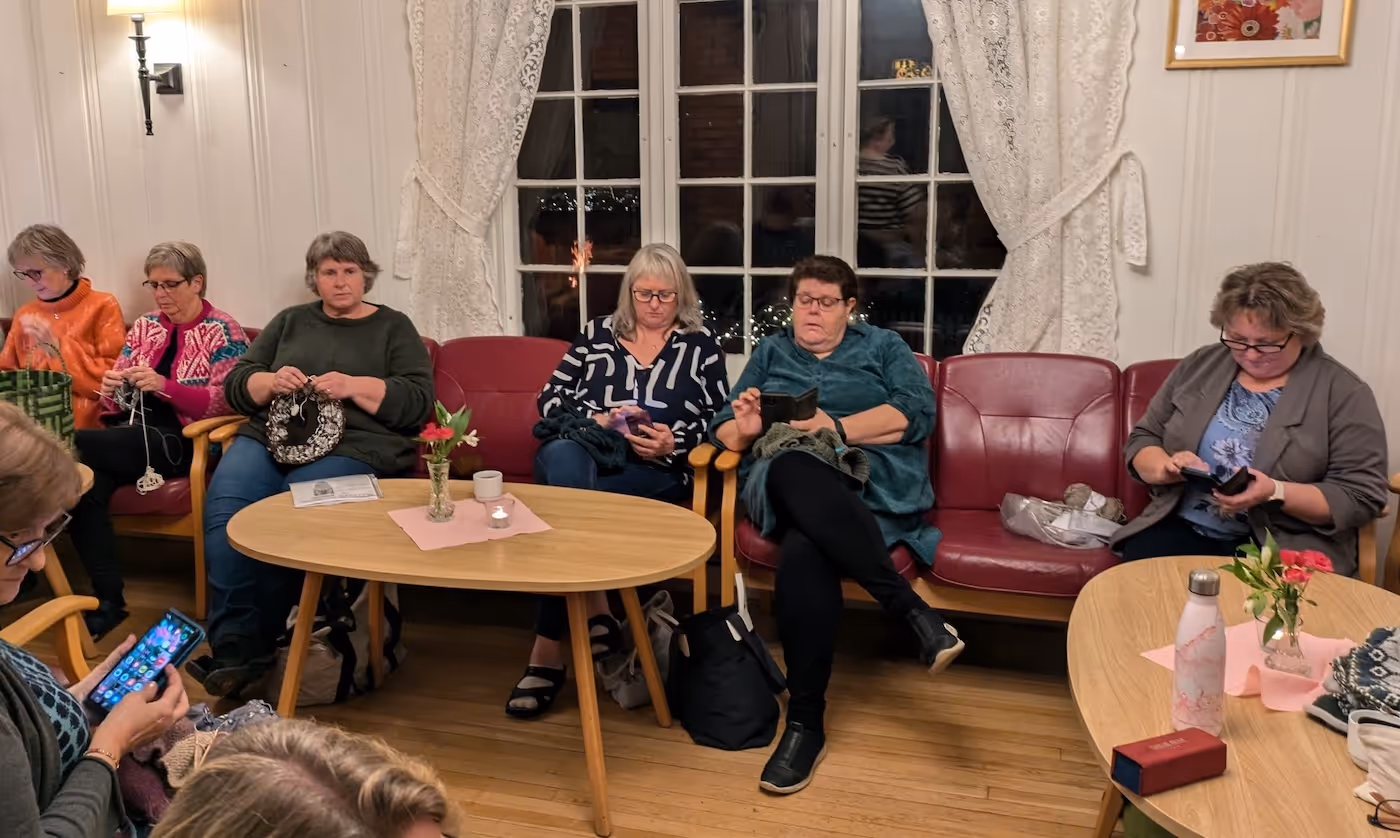 Bildet viser seks kvinner som sitter i en sofa og strikker