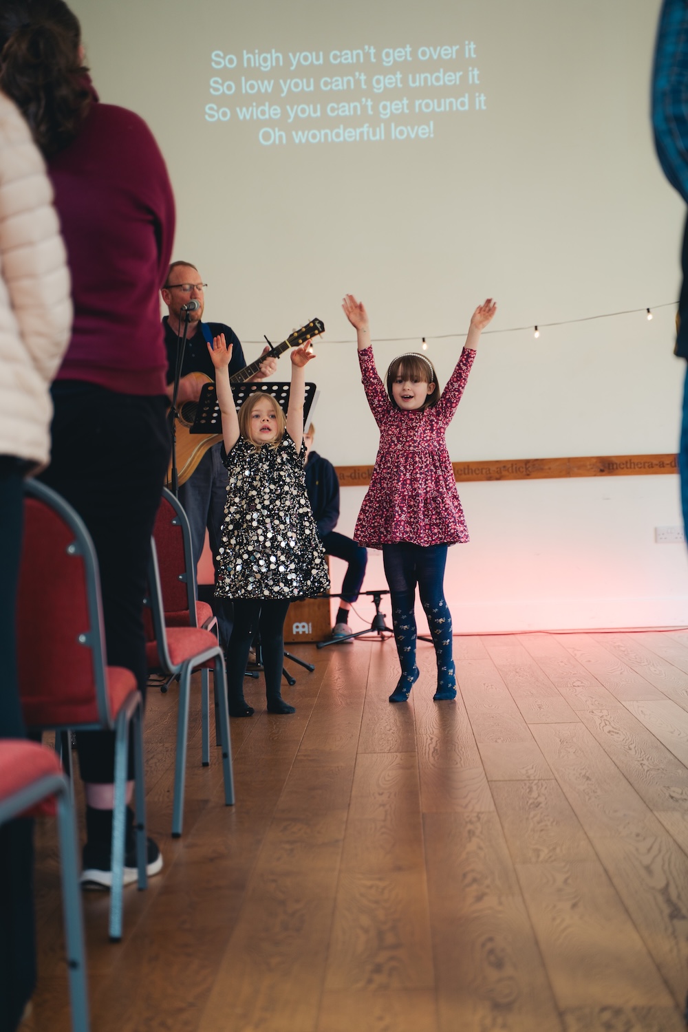 Bildet viser to unge jenter som smiler og danser foran en sangtekst foran en forsamling