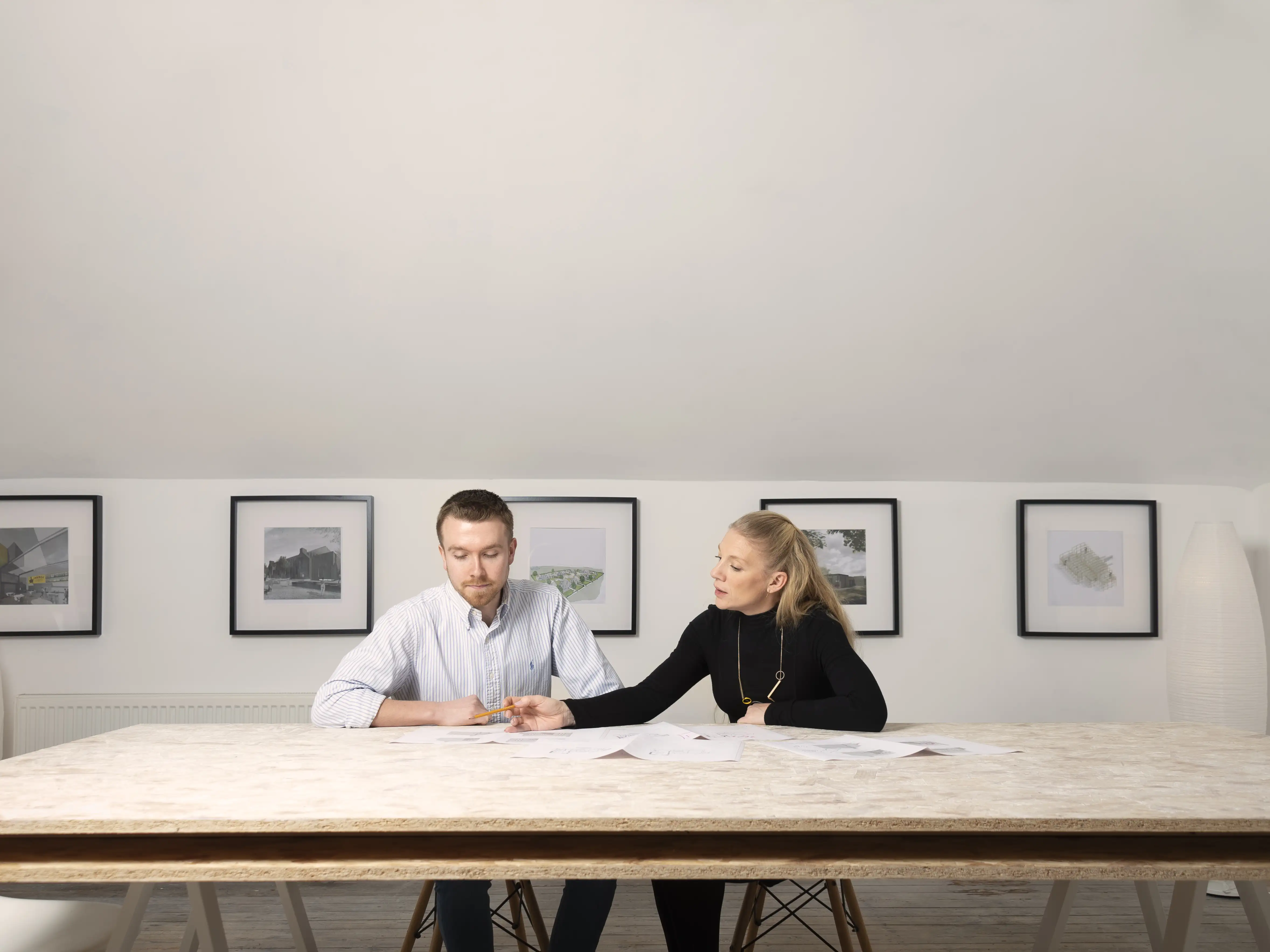 A landscape image in a light room of Laura and Jamie sat at a large desk discussing building plans