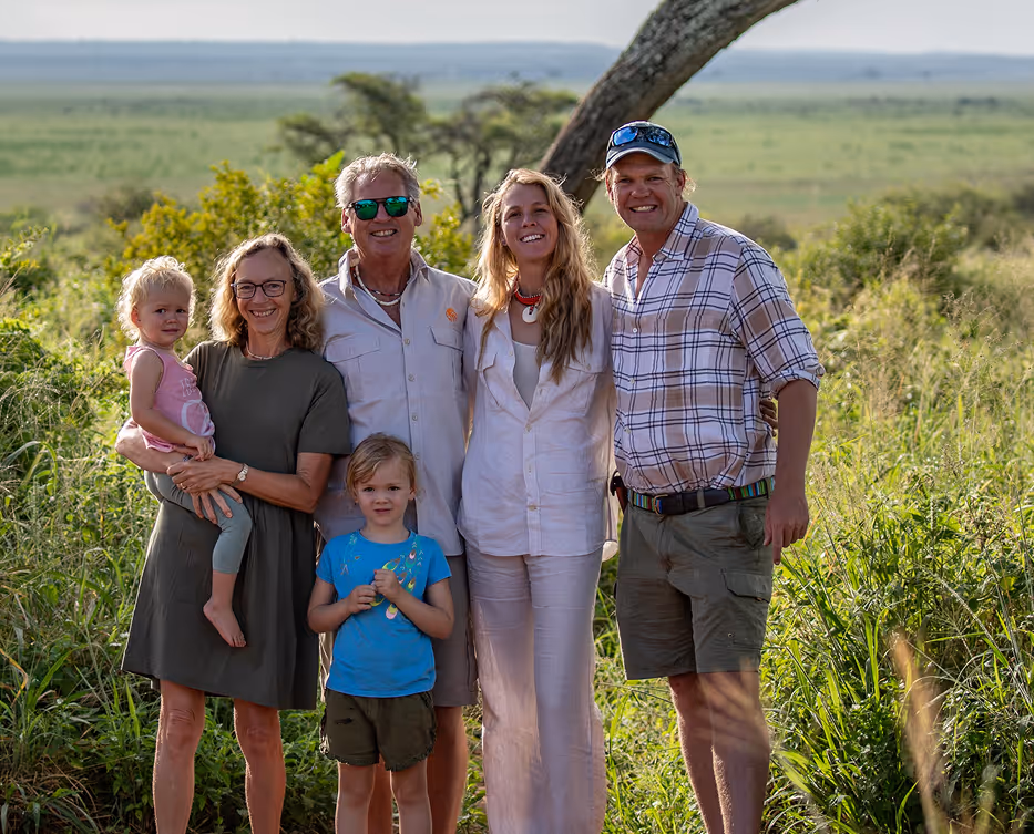 Happy family smiling together in a scenic savannah landscape surrounded by trees.