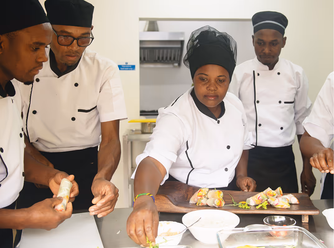 A team of professional chefs in a commercial kitchen led by a senior woman.