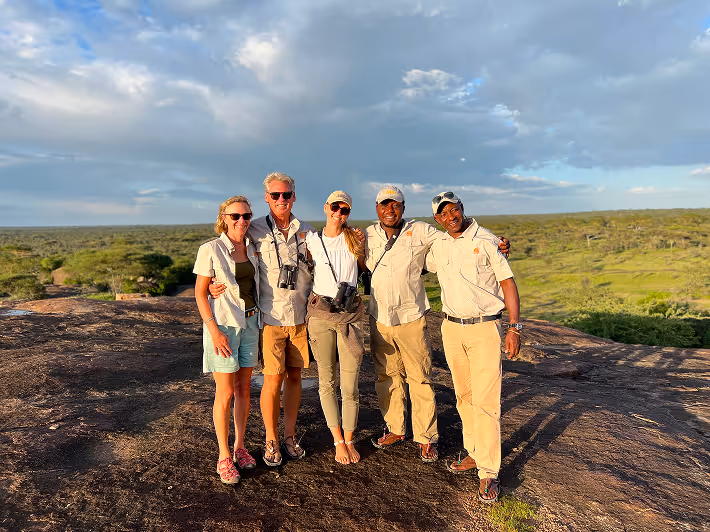 Wildlife safari tourists pose with binoculars on rocky savannah outcrop in Africa landscape.