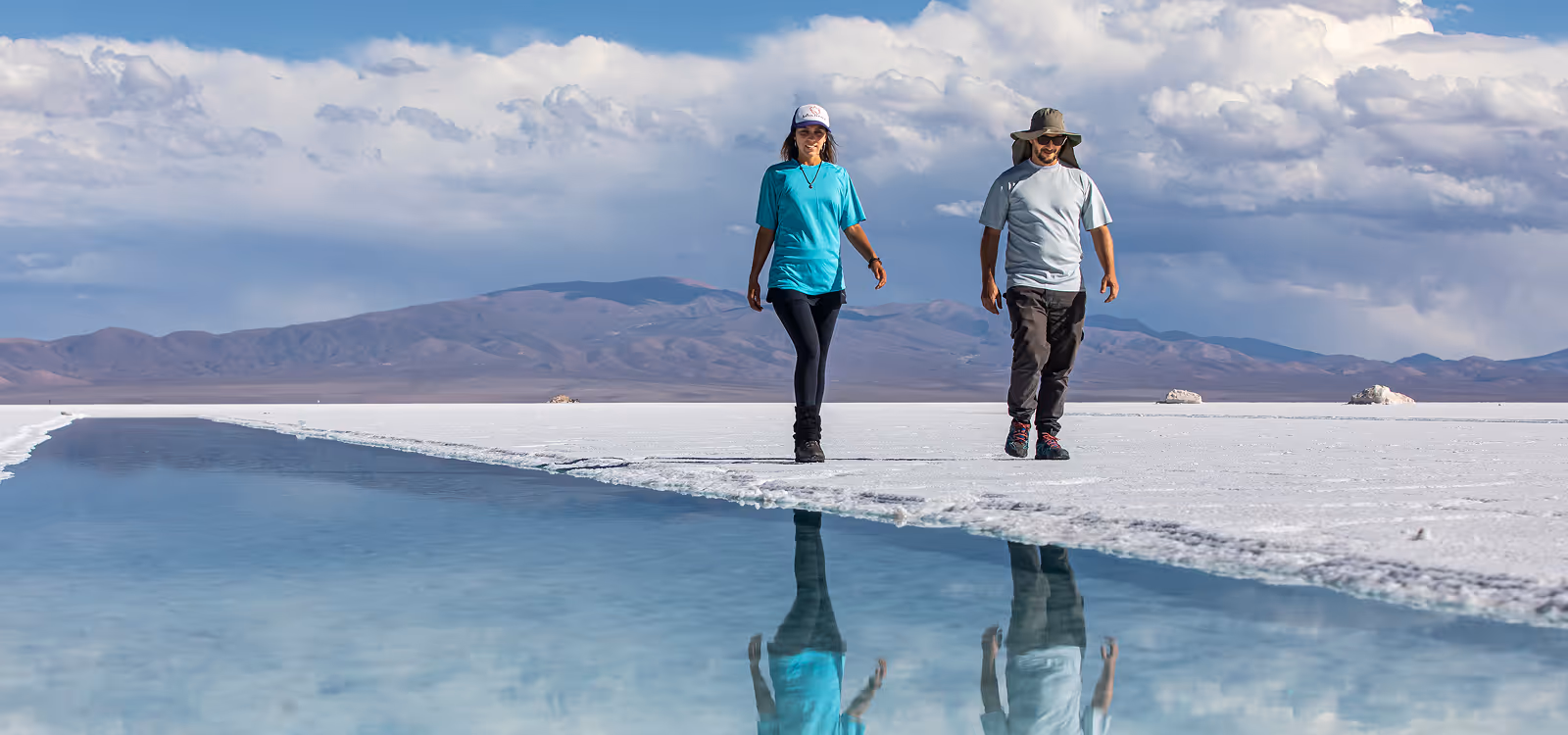 Romantic couple strolling on Salar de Uyuni, surrounded by majestic Andean mountains skyline.