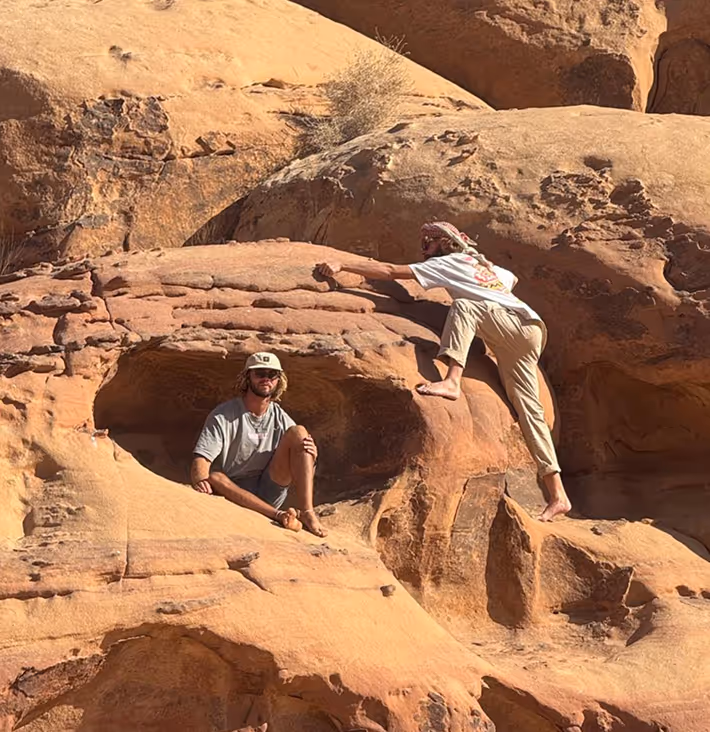 Two adventurous men climbing and sitting on an orange rocky desert formation together outdoor.