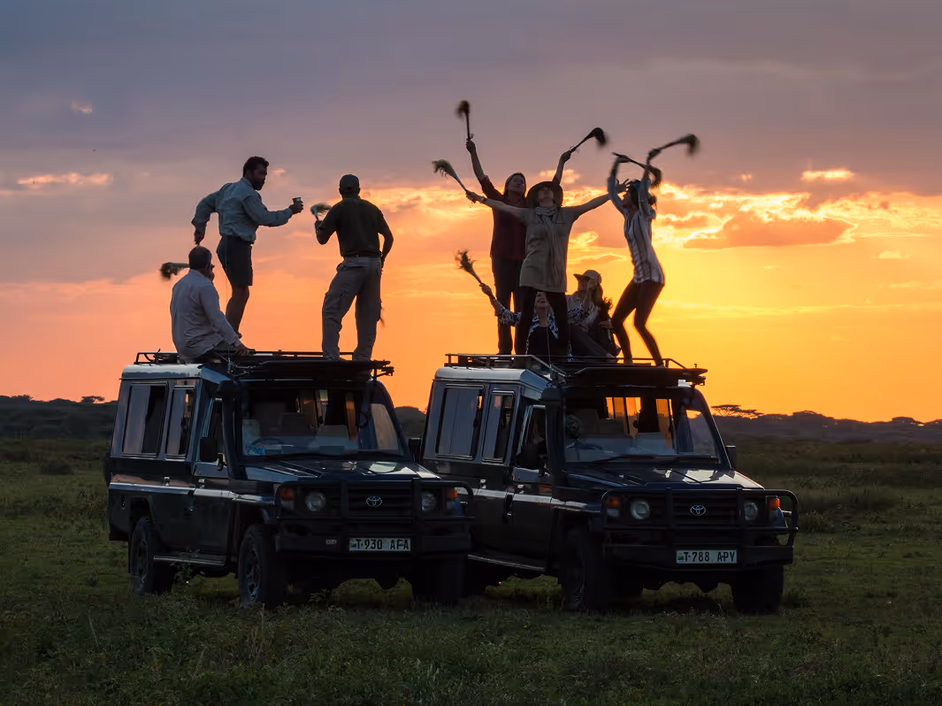 People on safari enjoying vibrant sunset with colorful feathers in African savannah landscape.