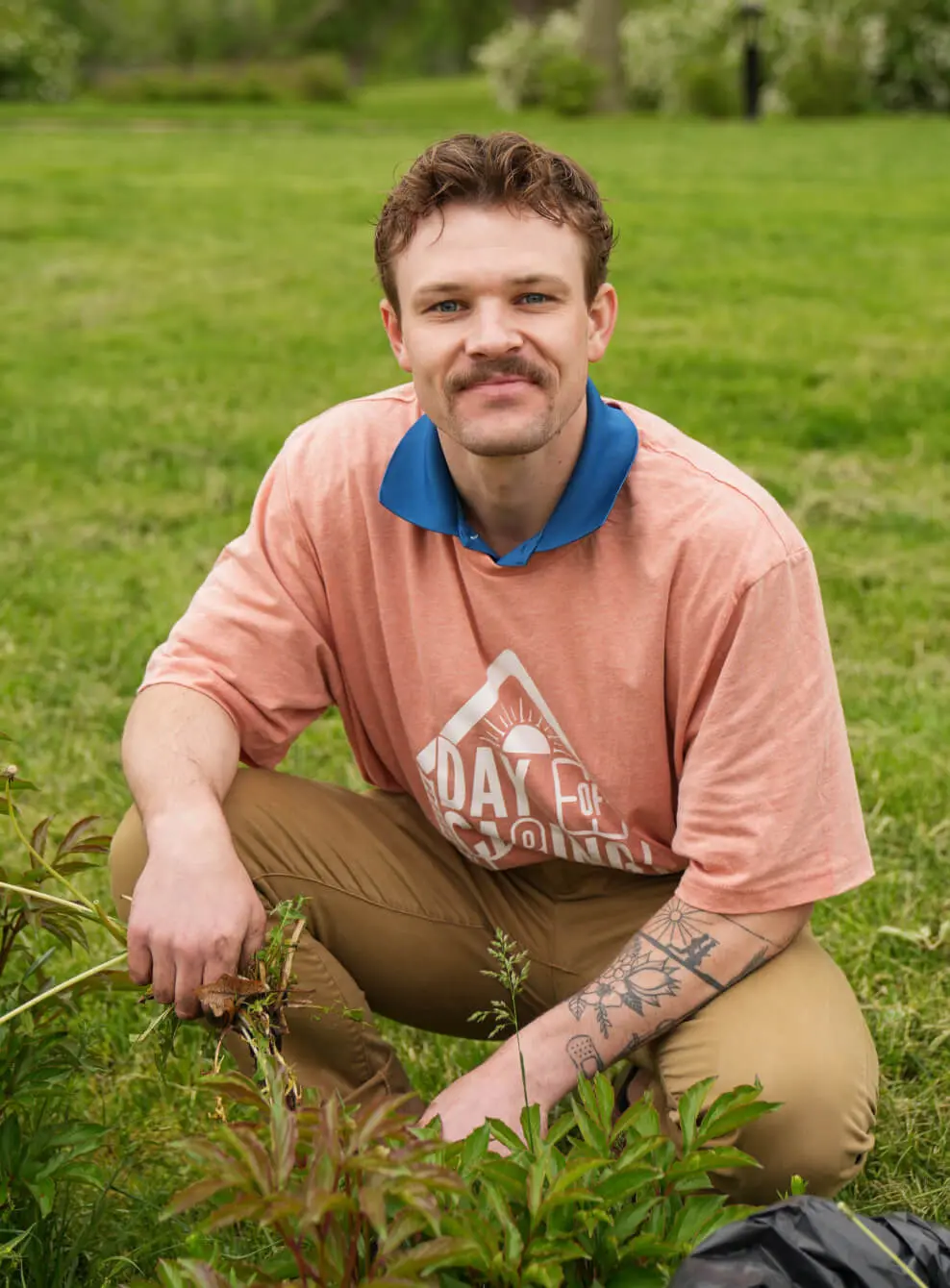 Man sitting on grass with hands clasped, looking at camera.