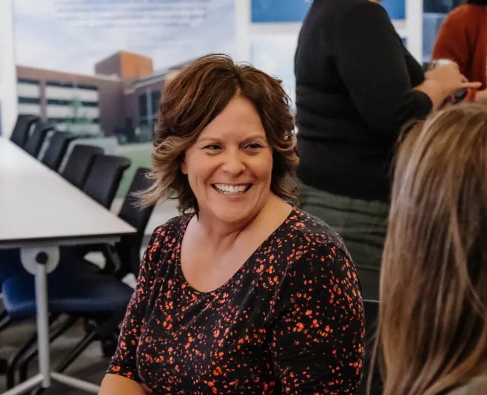 Woman smiling in a cafeteria or office break room.