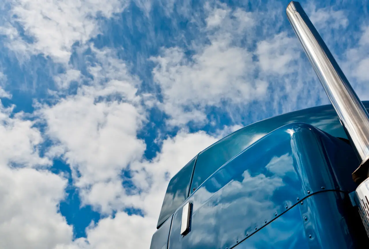 Blue semi-truck viewed from a low angle with sky in background.