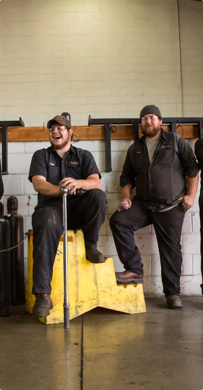 Three people posing indoors, possibly warehouse or facility.