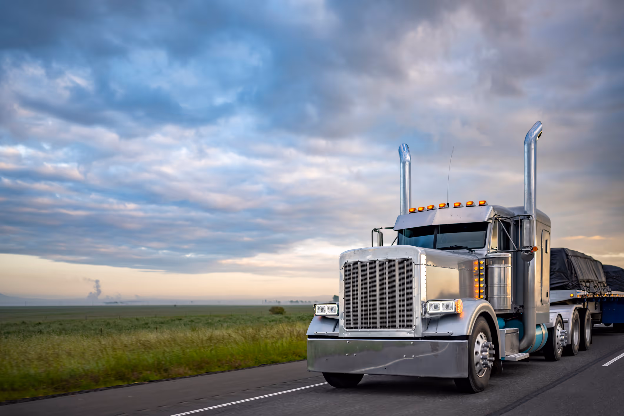 semi truck driving on the road in front of an open field