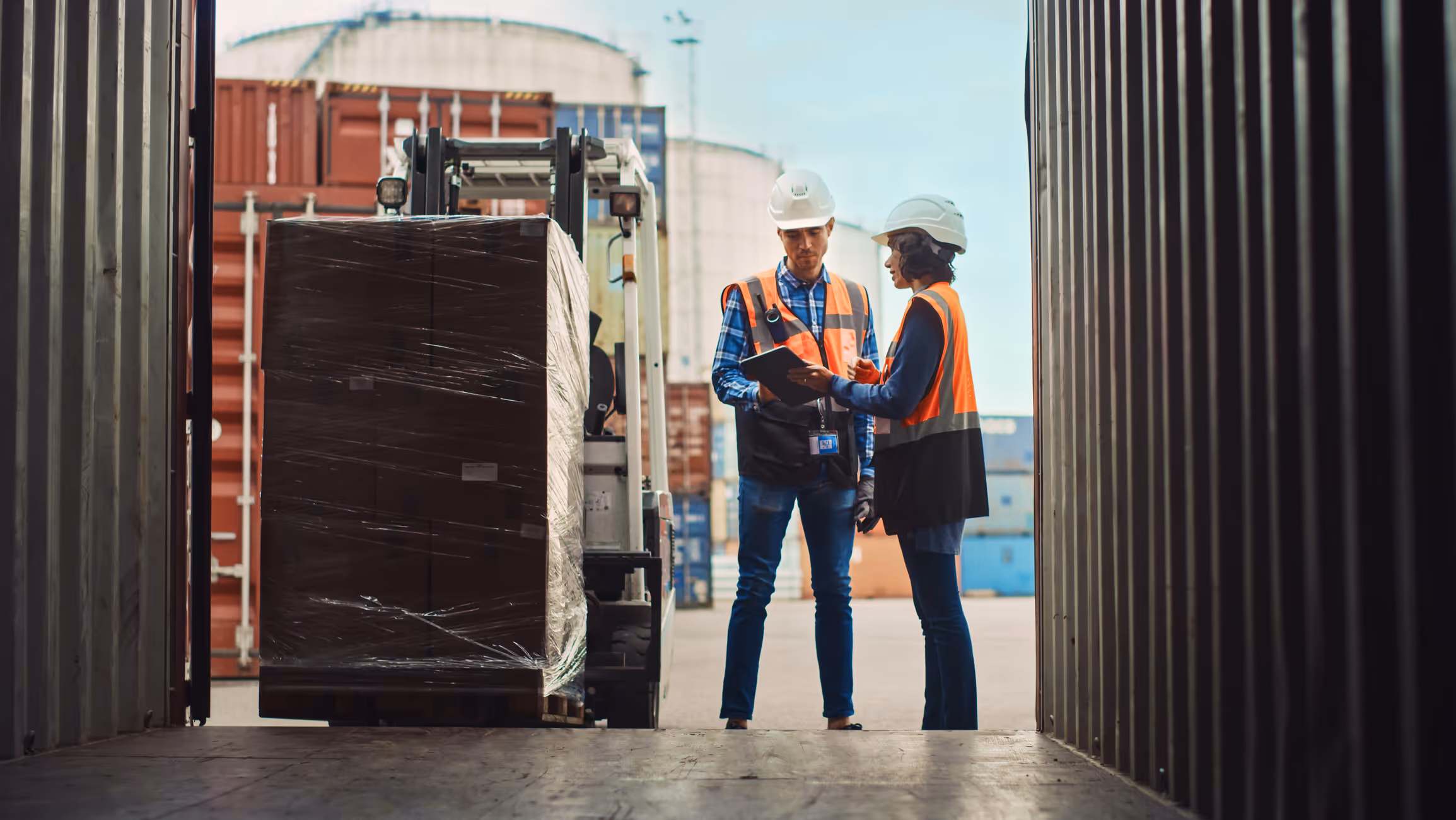 two workers wearing hard hats standing next to a fork lift