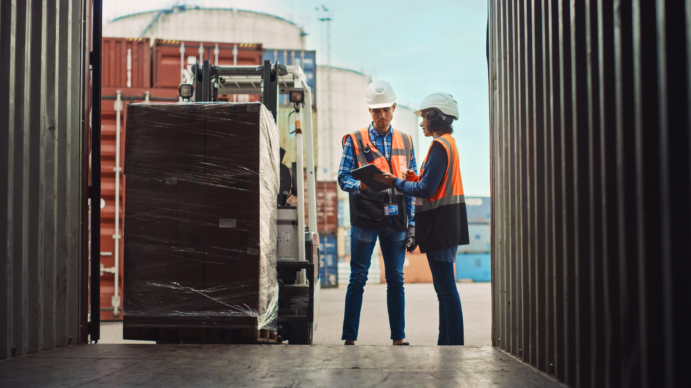 two workers wearing hard hats standing next to a fork lift