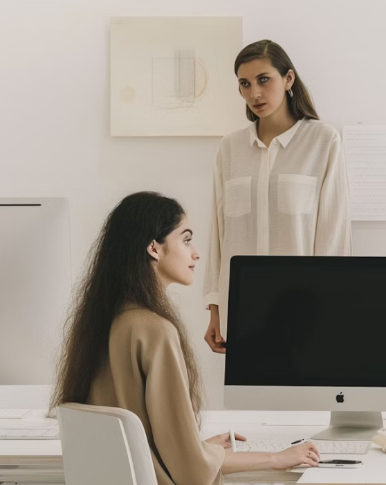 Two women in an office collaborating while examining a computer screen together.