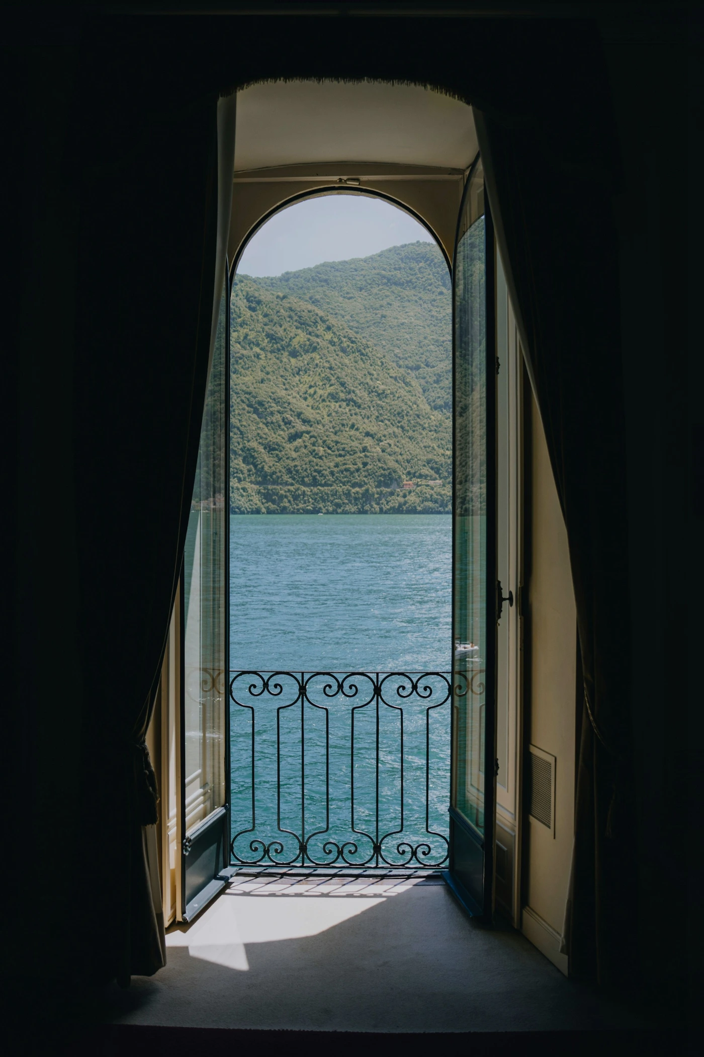 Open arched doorway with ornate iron railing overlooking a blue lake and green forested hills.
