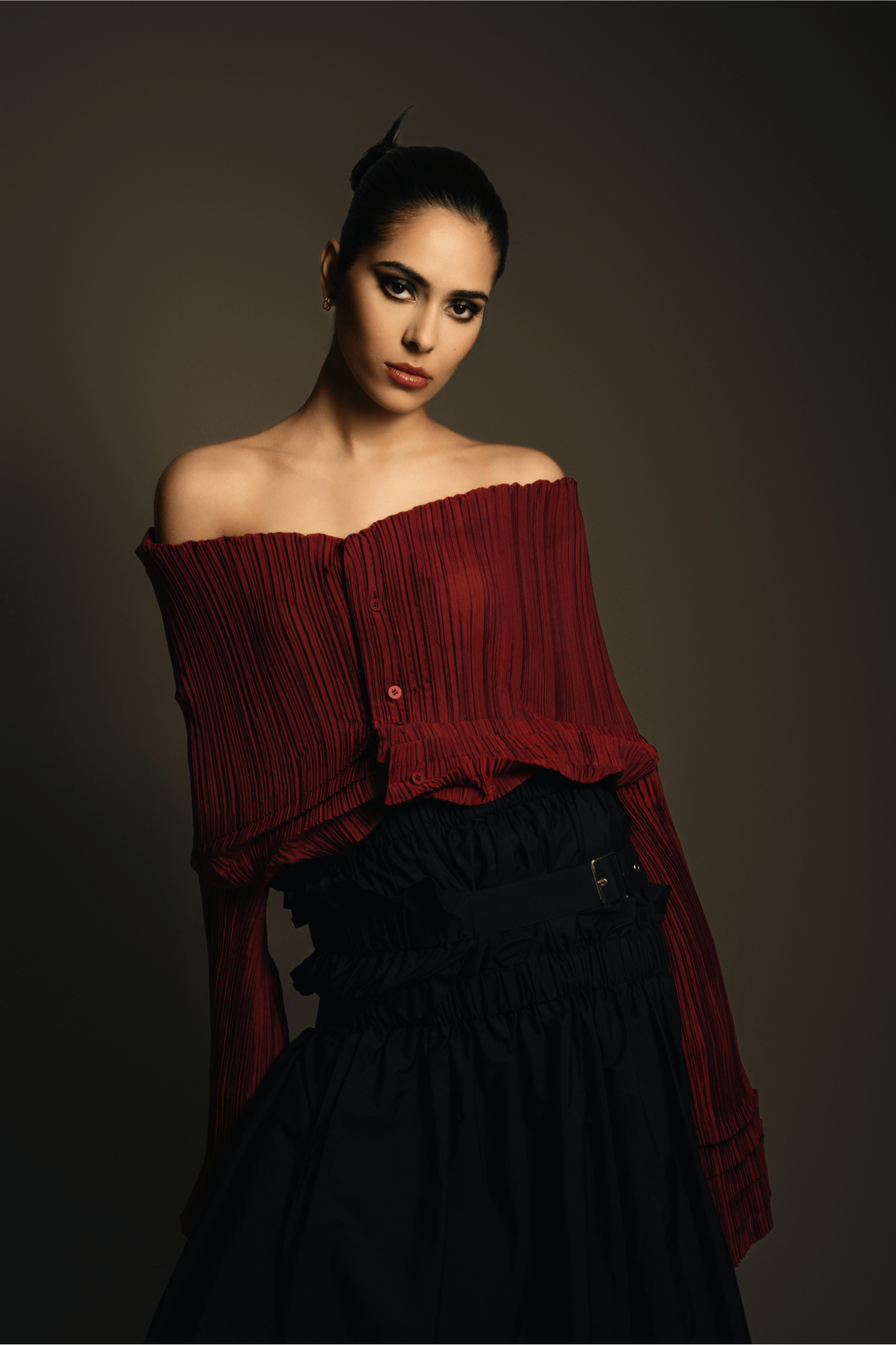 A fashion-forward model in a deep dark cherry pleated off-shoulder blouse and high-waisted black skirt, capturing the essence of the 2025 trend that celebrates rich burgundy hues in modern silhouettes.
