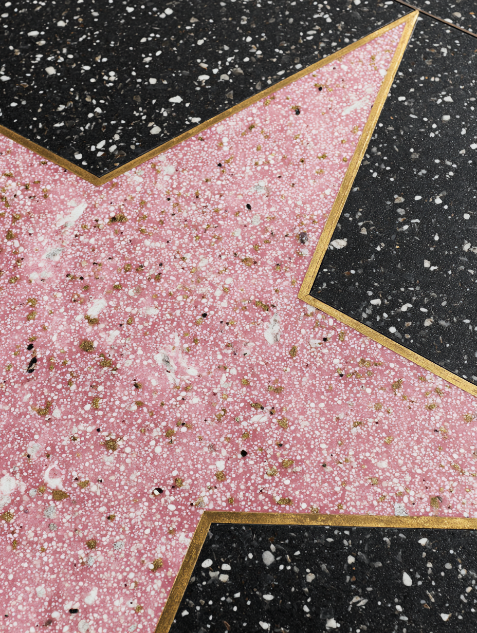 Close-up of a blank pink star with a gold border on the Hollywood Walk of Fame, surrounded by black speckled terrazzo tiles.