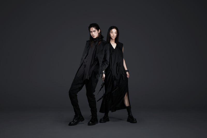 Two members of the fashion label NINJA TOKYO pose in coordinated, all-black avant-garde outfits against a dark background — showcasing sharp tailoring, layered silhouettes, and modern Japanese minimalism.