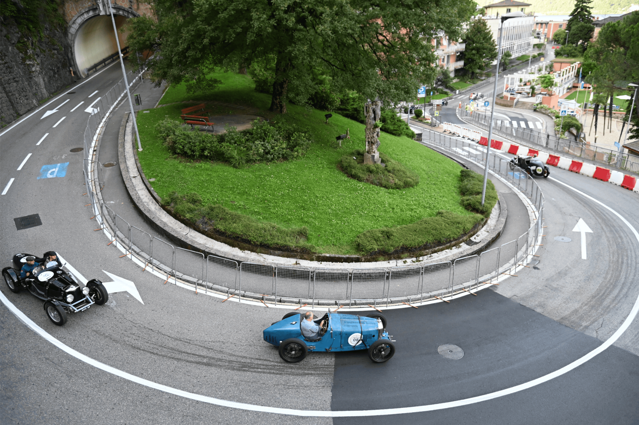 Classic racing cars, including a blue Bugatti, navigate a sharp hairpin turn near a tunnel on the historic Campione street circuit during the 2025 revival.