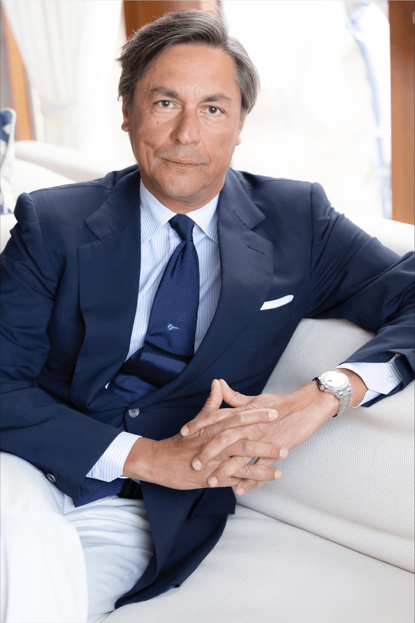 Portrait of Andrea Recordati, Commodore of the Yacht Club Costa Smeralda, dressed in a navy suit and tie, seated indoors and wearing a Rolex watch.
