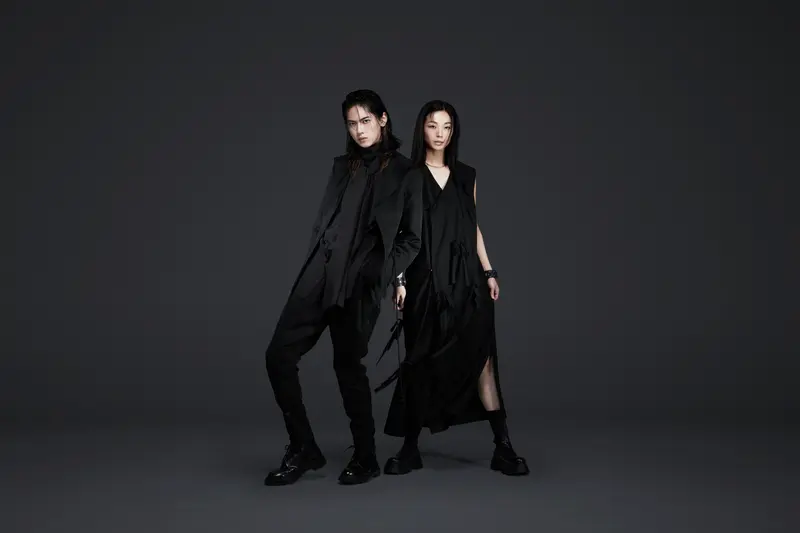 Two members of the fashion label NINJA TOKYO pose in coordinated, all-black avant-garde outfits against a dark background — showcasing sharp tailoring, layered silhouettes, and modern Japanese minimalism.