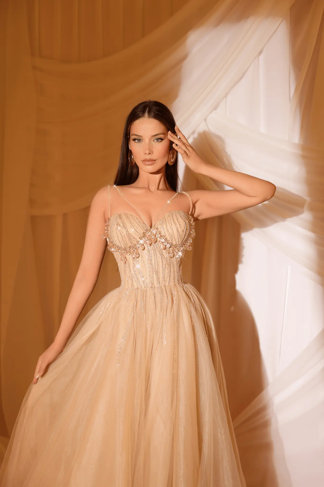 Model wearing an elegant gold-beige evening gown with sparkling embellishments and flowing tulle skirt.