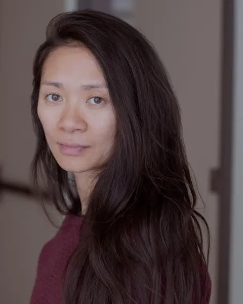 Portrait of filmmaker Chloé Zhao, director of Hamnet, wearing a burgundy sweater and looking calmly at the camera.
