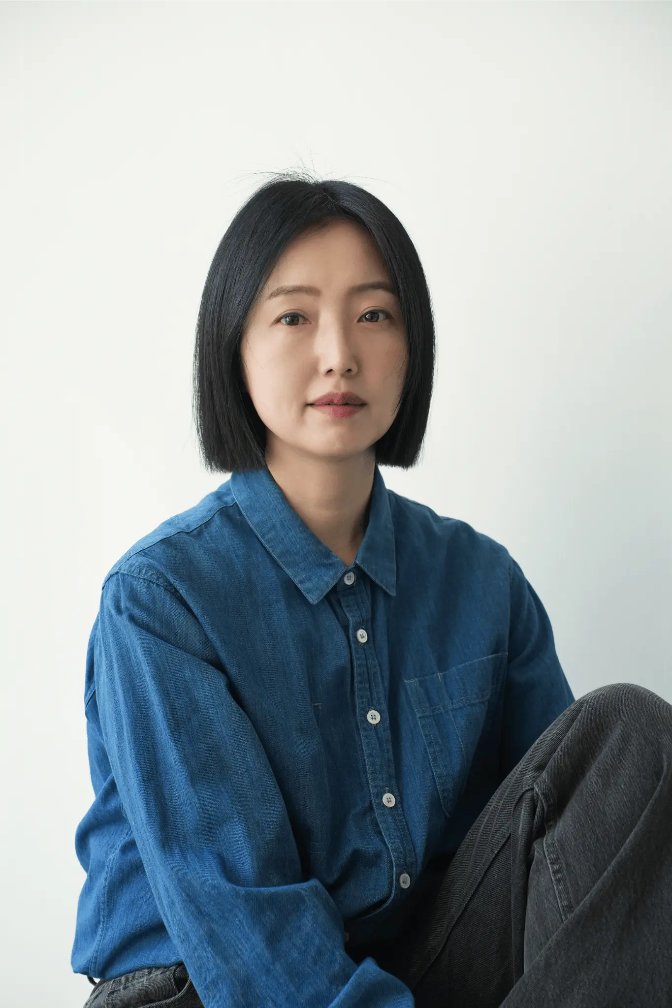 Portrait of Korean artist Im Youngzoo, winner of the Frieze Seoul 2025 Artist Award, wearing a denim shirt and seated against a minimalist white background.