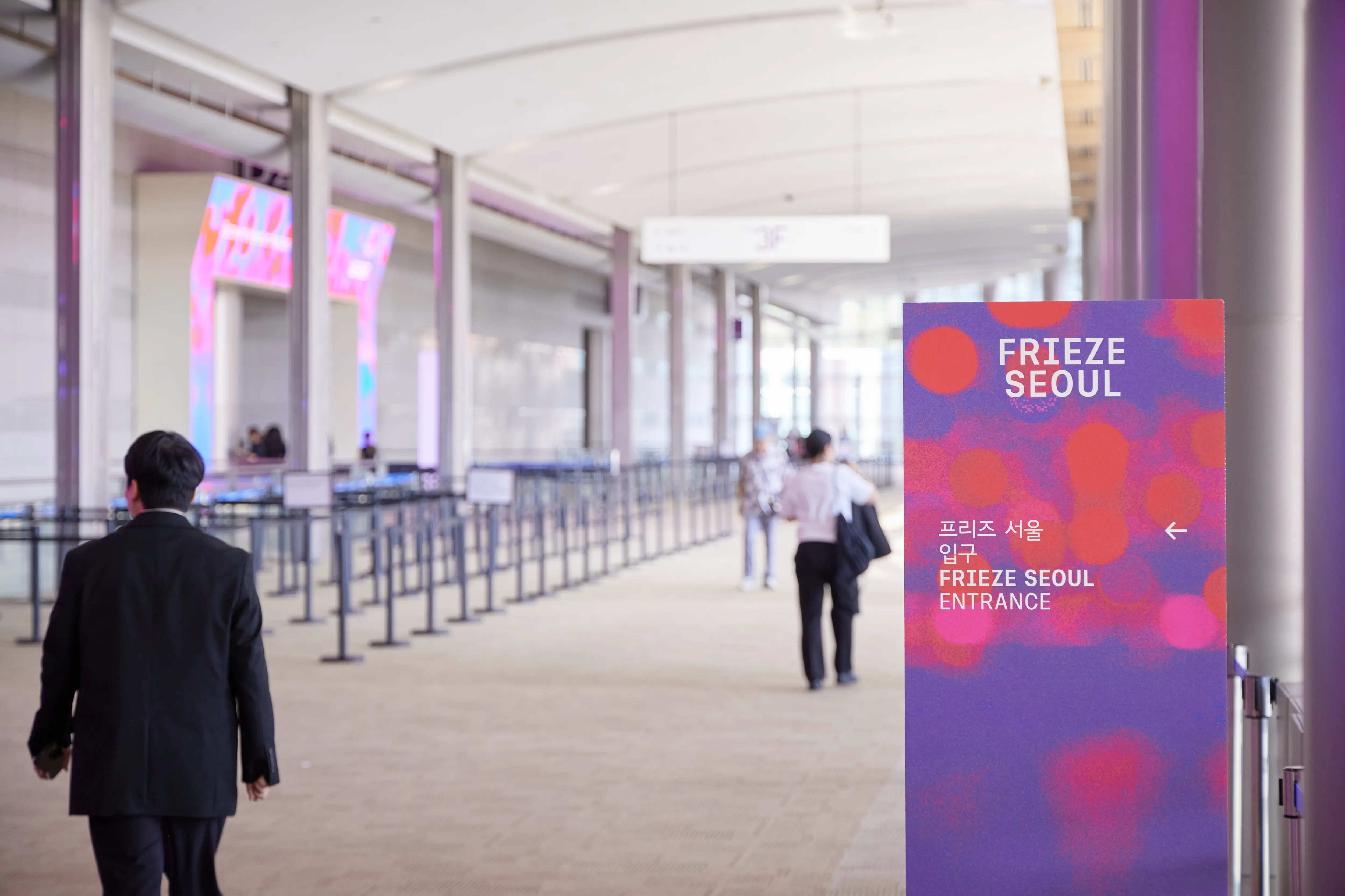 Directional entrance signage for Frieze Seoul 2025 at COEX in Gangnam, with visitors walking through the queue lines in a brightly lit exhibition hall.