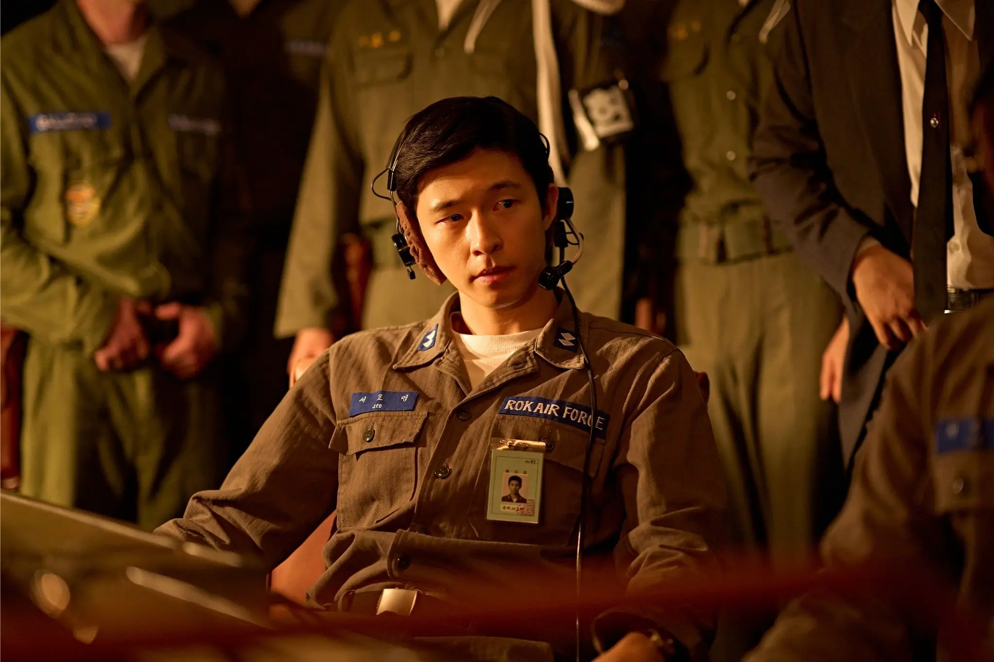 A Korean Air Force officer wearing a headset sits in a tense command room surrounded by military personnel, in a dramatic moment from Byun Sung-hyun’s film Good News, premiered at the 50th Toronto International Film Festival (TIFF).