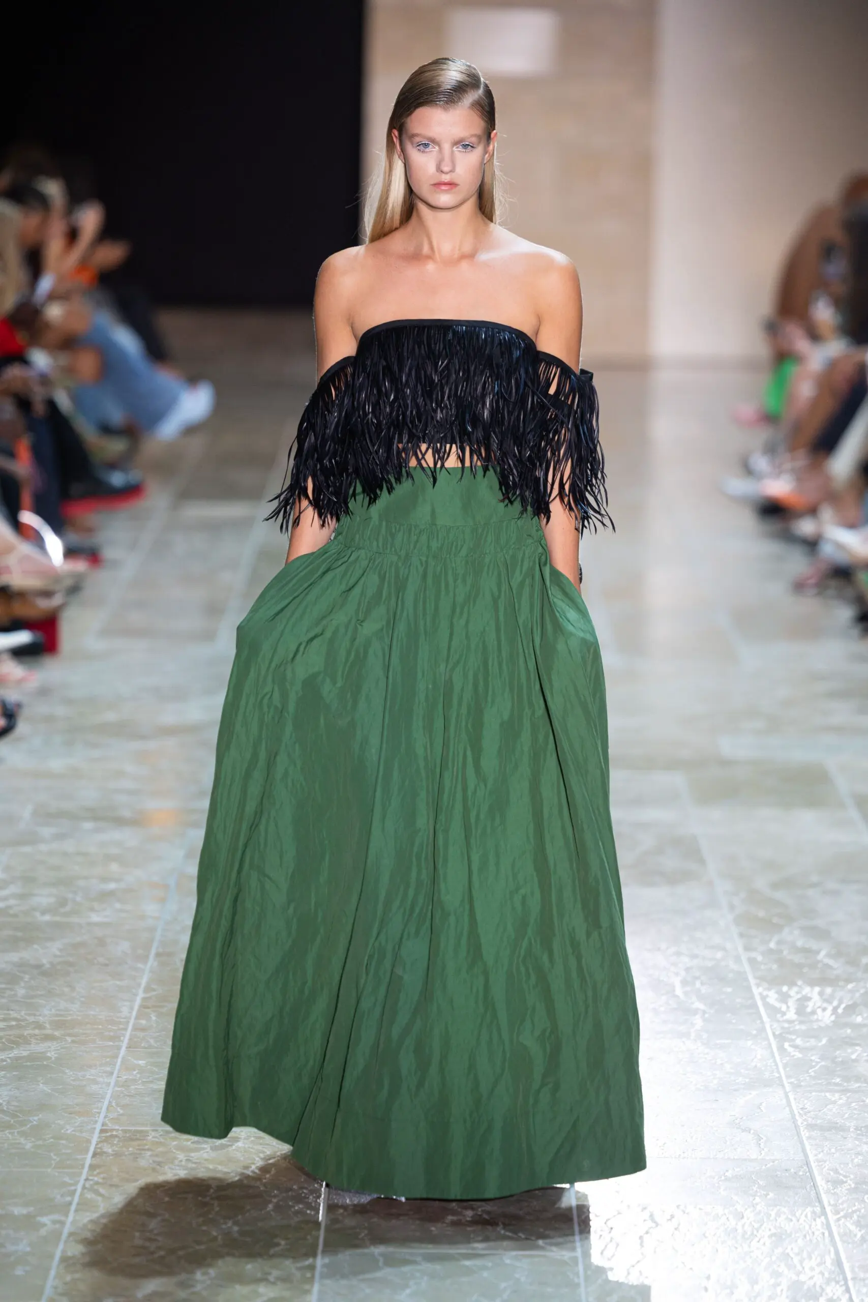 A model walks the runway in a NATAN ensemble featuring a voluminous green skirt and a strapless black fringe top, blending classic elegance with modern texture at Amsterdam Fashion Week.