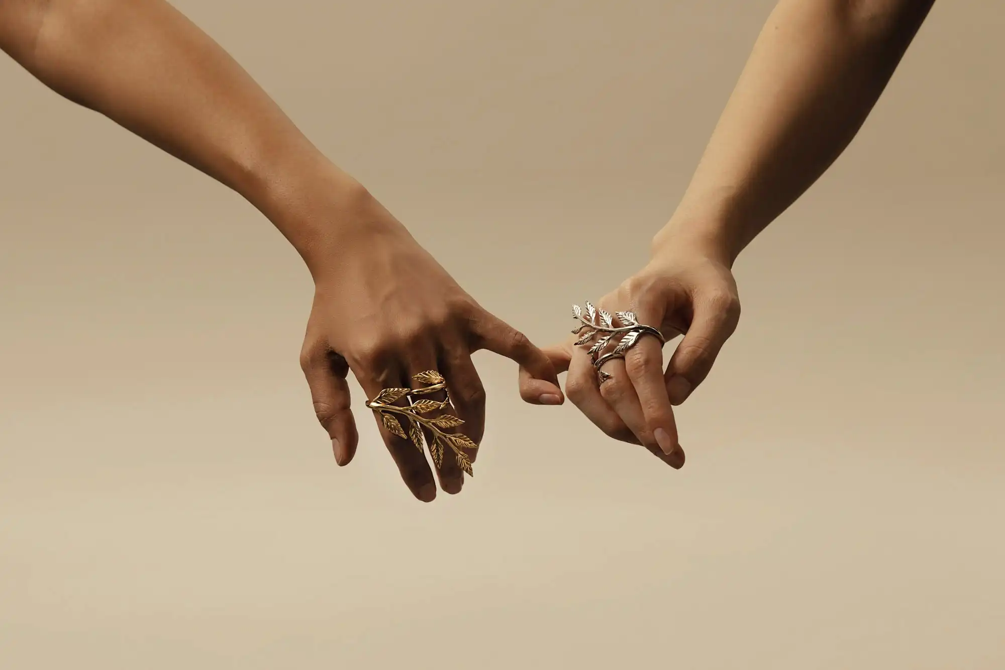 Two hands gently touching fingers, each adorned with gold and silver laurel rings from Le Sable's Pep Talk jewelry line.
