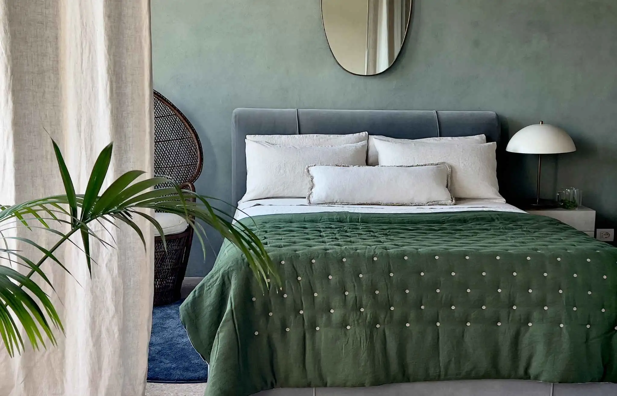 A serene bedroom styled with Once Milano’s green hand-embroidered quilt and cream fringed linen pillows, showcasing refined Italian craftsmanship and understated luxury.