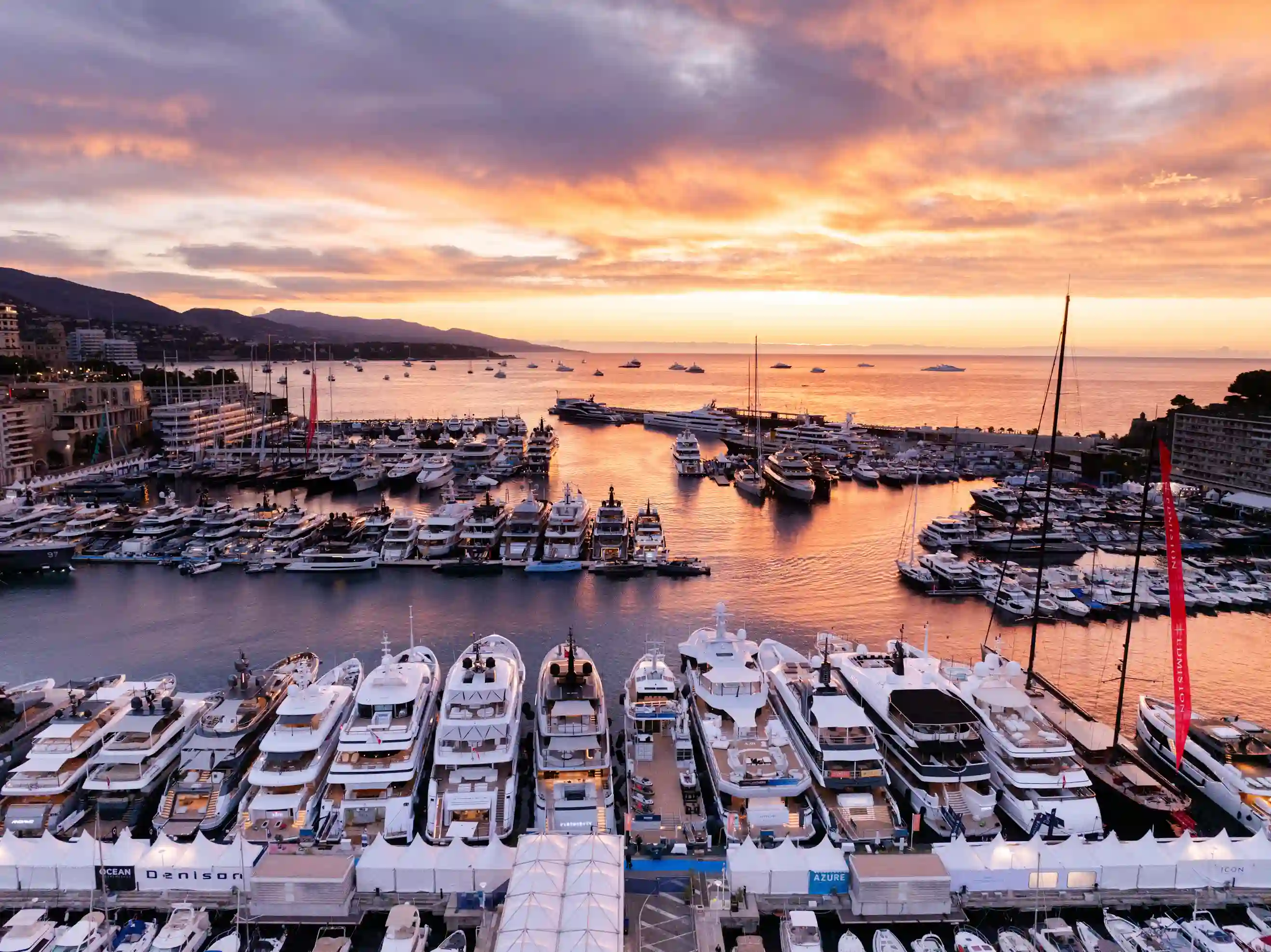 A panoramic view of superyachts moored at Port Hercule in Monaco during sunset, with the harbor bathed in golden light at the 2025 Monaco Yacht Show.