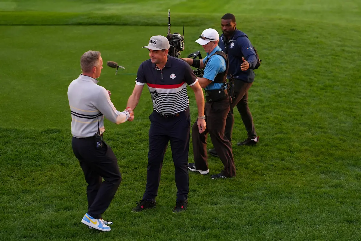 Team Europe captain Luke Donald shakes hands with Team USA captain Keegan Bradley at Bethpage Black during the 2025 Ryder Cup, as camera crews capture the moment of sportsmanship on the course.