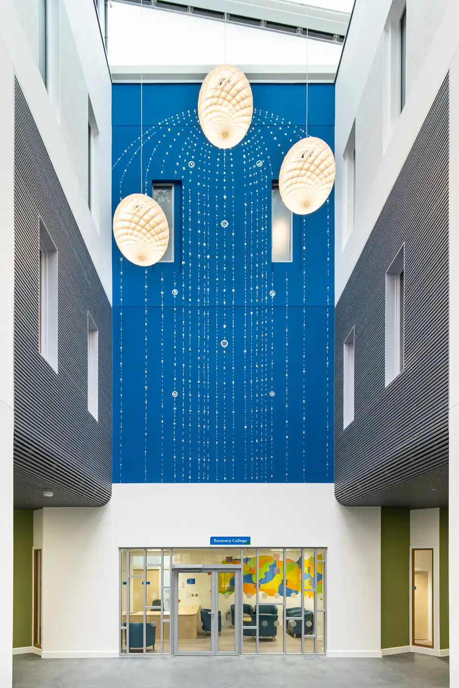 Atrium installation by Sutapa Biswas at Springfield Hospital (2023), featuring a deep blue wall with intricate white dotted patterns and large shell-shaped hanging lights above the entrance to the Recovery College.