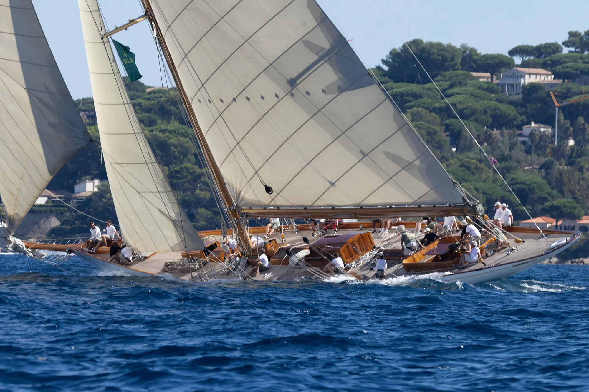 Crew sails elegant vintage wooden yachts with cream-colored sails during a close race at Les Voiles de Saint-Tropez 2025 on the French Riviera.
