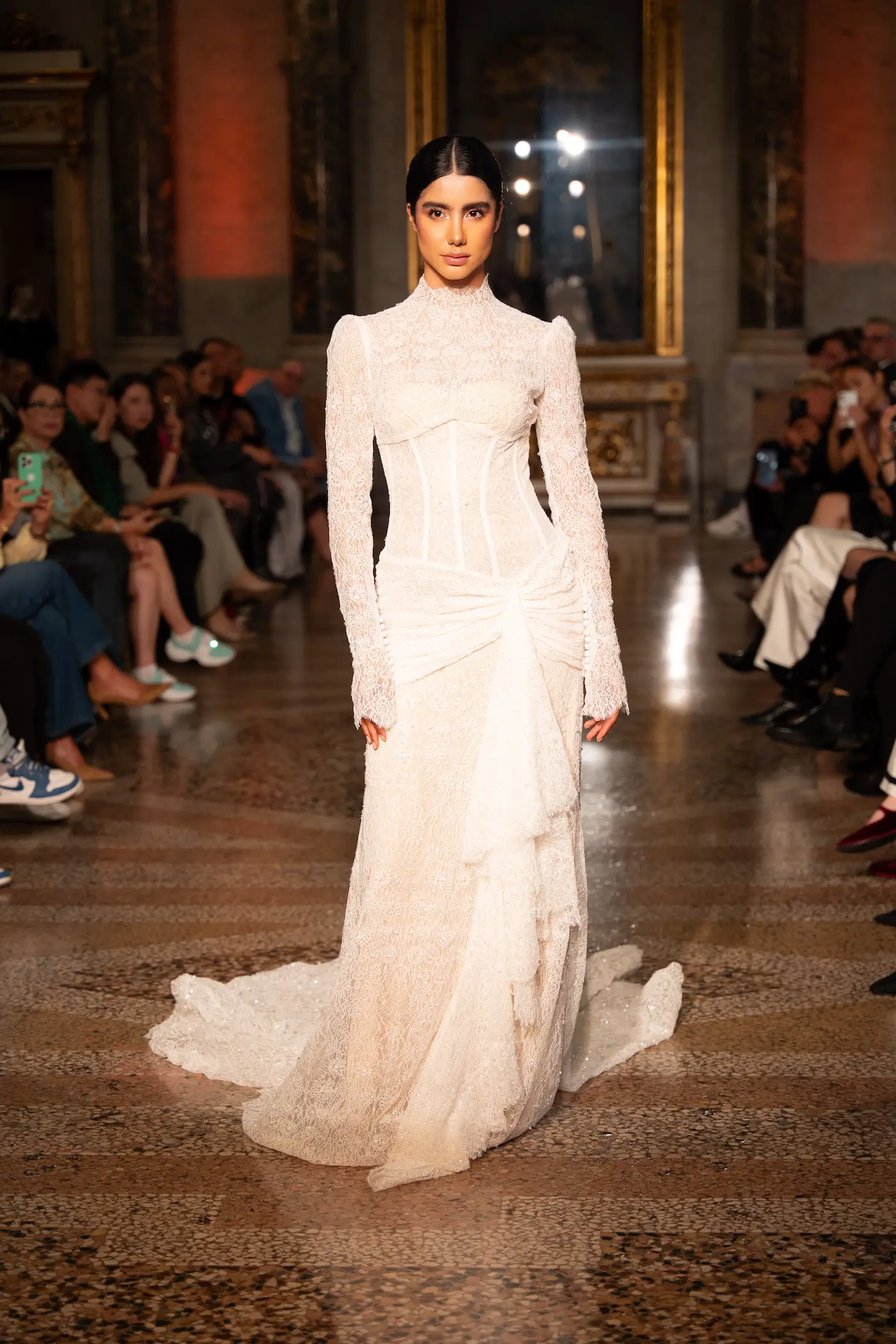 Model in a white high-neck lace bridal gown with corset detailing and ruched skirt, embodying timeless elegance.