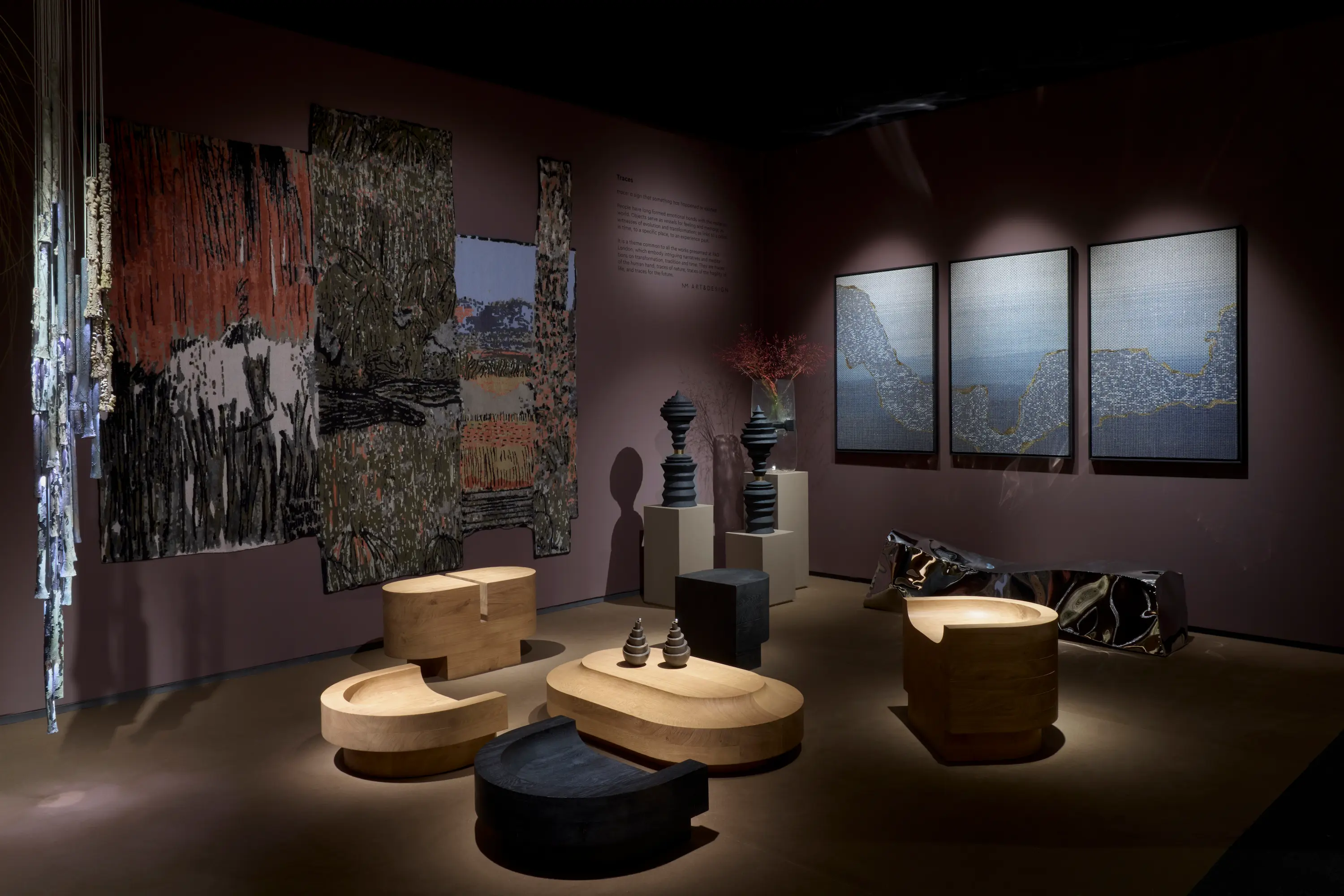 A dimly lit booth by Rademakers Gallery at PAD London 2025 featuring sustainable artworks, including woven tapestries, sculptural furniture, and abstract wall art, highlighting eco-conscious craftsmanship and contemporary Dutch design.