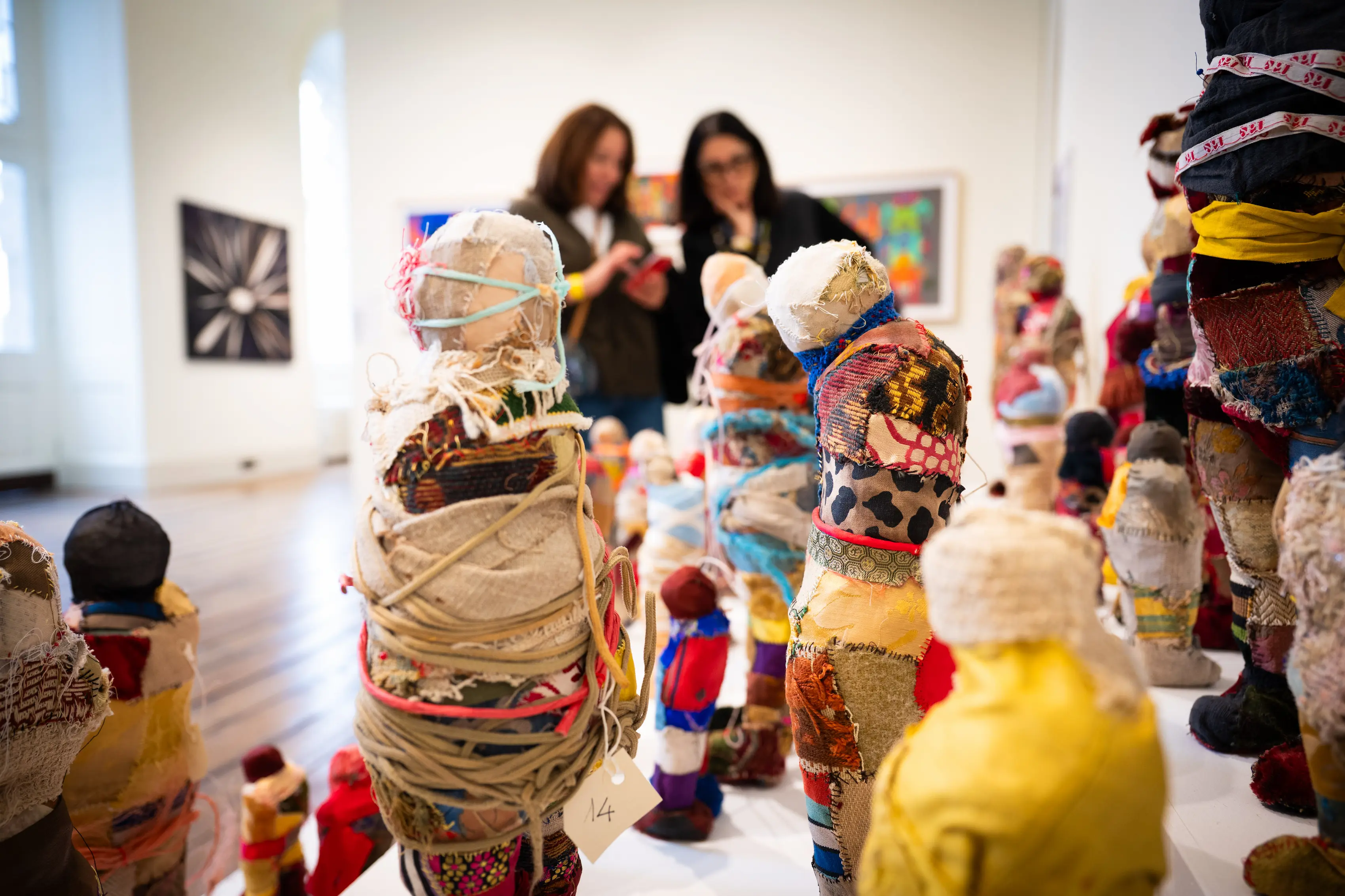 Colorful textile and fabric-wrapped sculptures displayed at 1-54 Contemporary African Art Fair London 2025, with visitors observing the artworks in the background, showcasing craftsmanship and cultural storytelling through mixed materials.